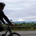 Biker im Vordergrund mit Blick auf eine schnebedeckte Vulkanspitze in der Seenregion Chile