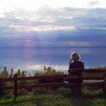 Frau sitzt in der Abenddämmerung auf Bank am See, mit Blick zum See